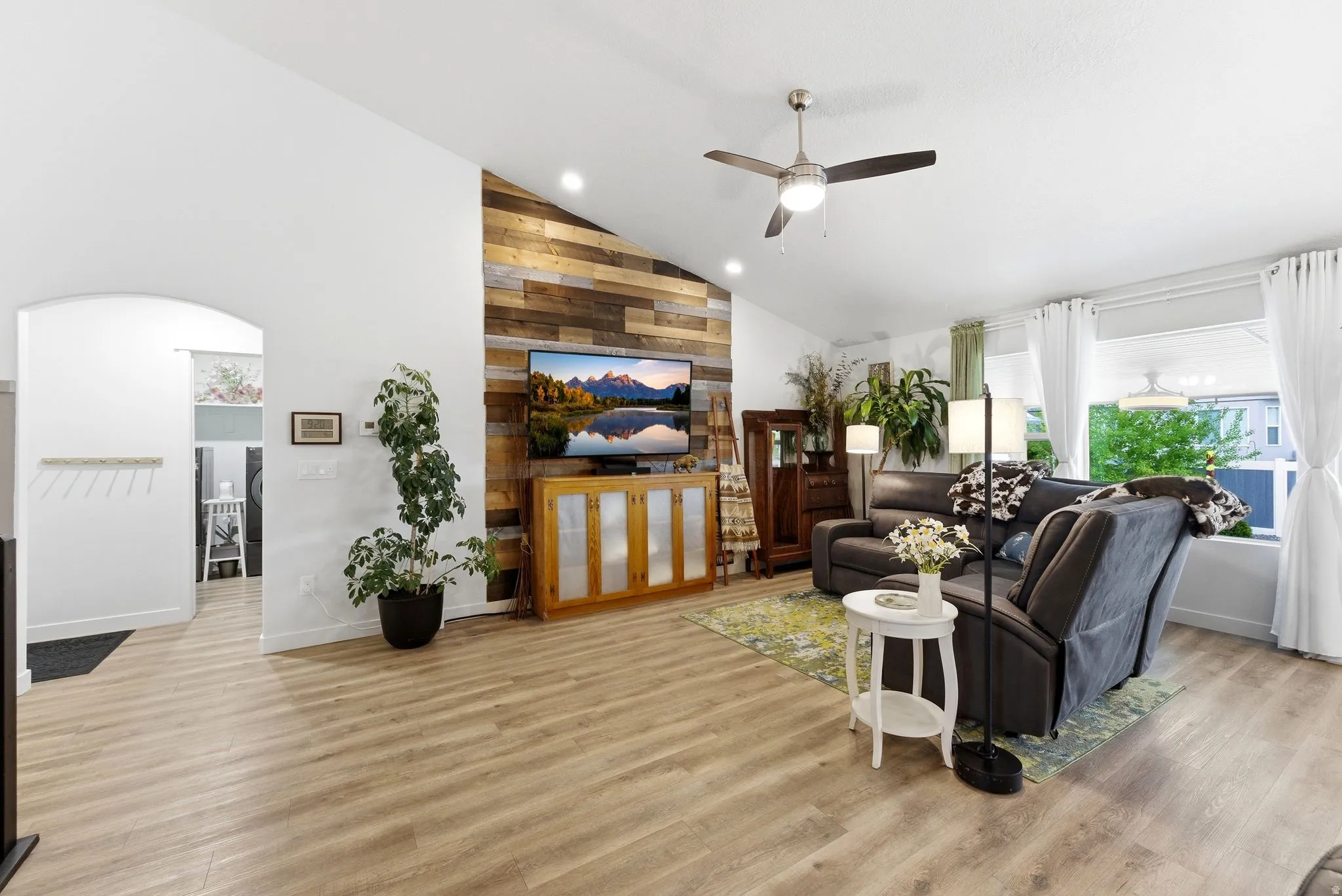 Living room with vaulted ceiling, a ceiling fan, light wood-style floors, recessed lighting, and wooden walls