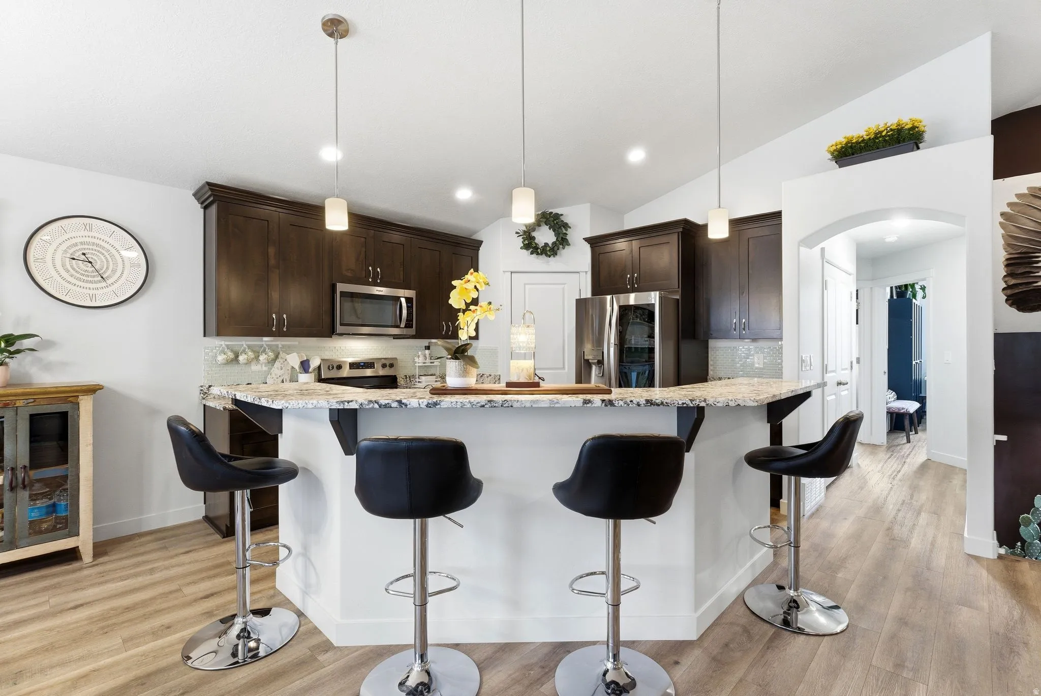 Kitchen with decorative backsplash, lofted ceiling, light stone counters, arched walkways, and a breakfast bar