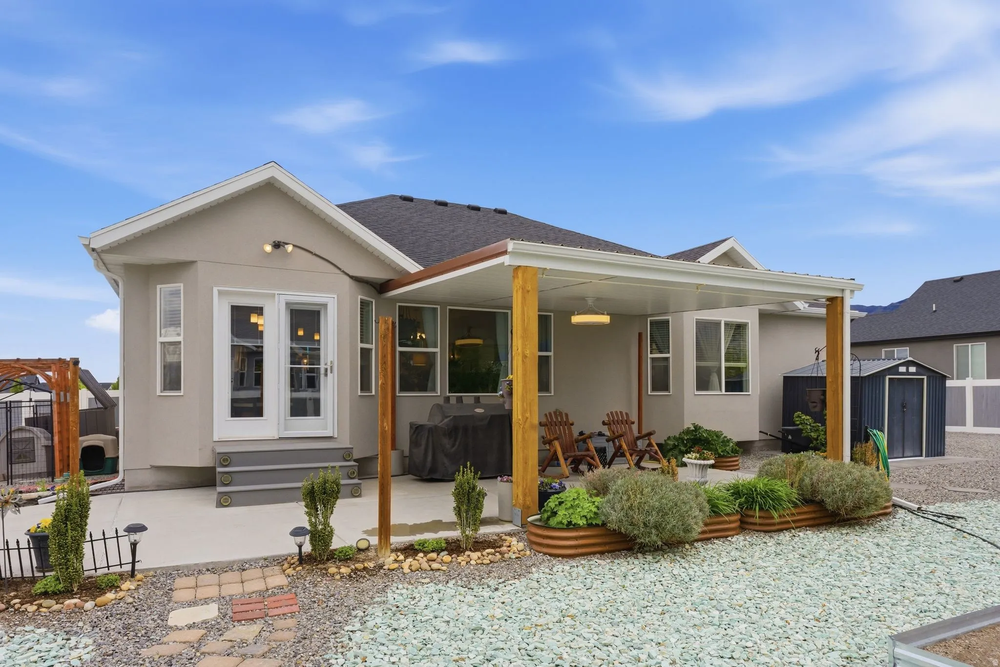 View of front of property with a storage shed, stucco siding, a patio, and a shingled roof