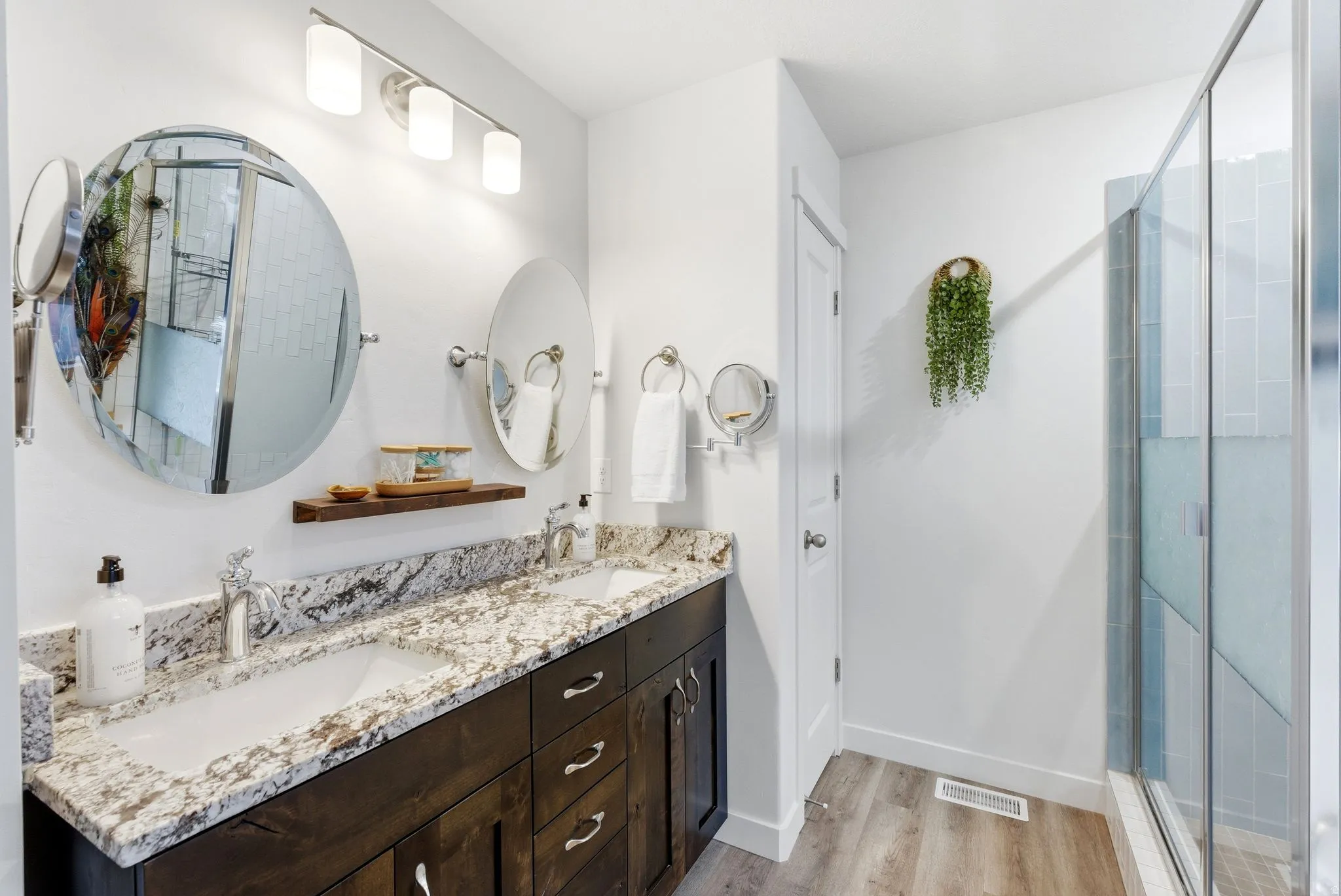 Bathroom with double vanity, light wood finished floors, and a stall shower