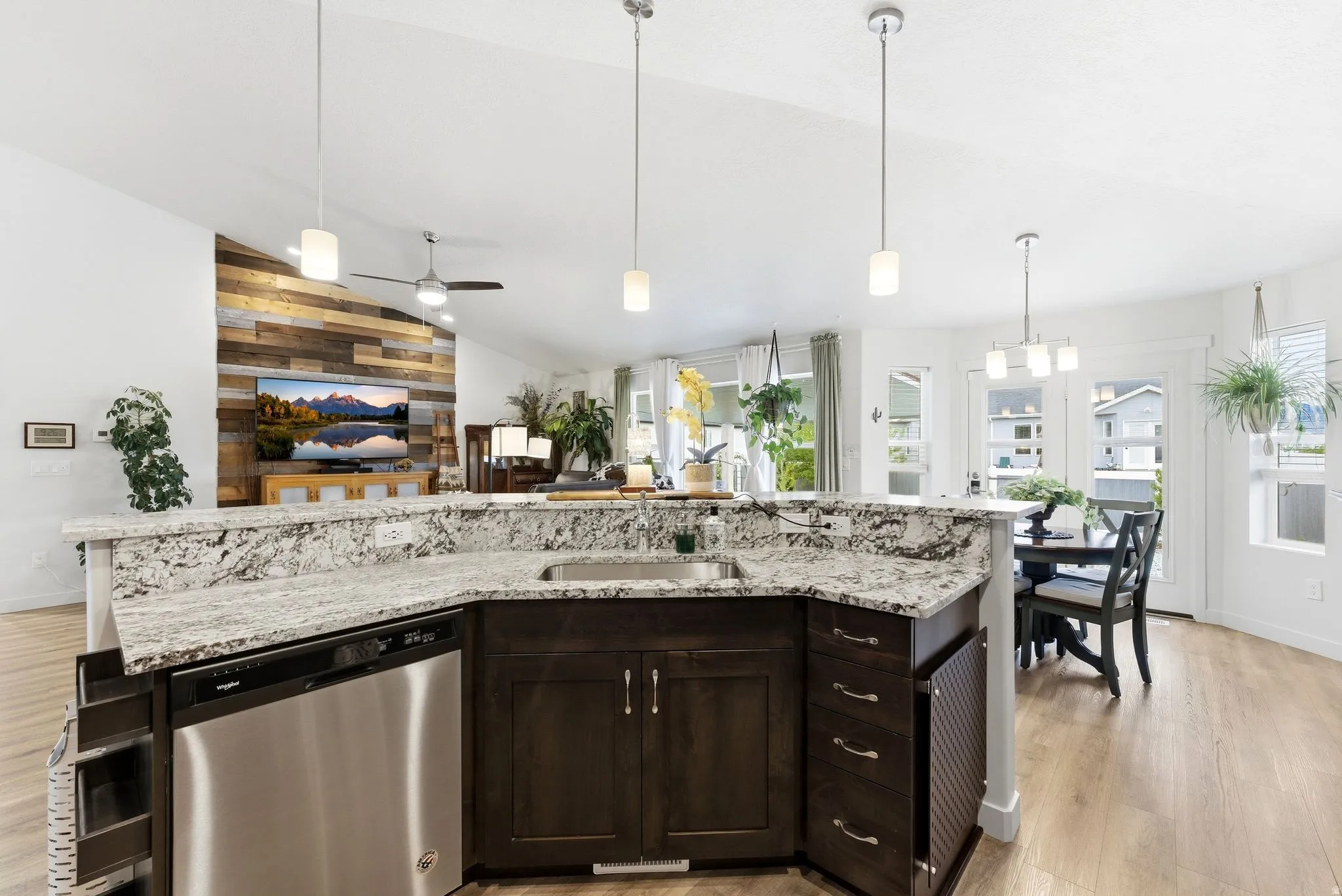 Kitchen featuring dark wood finish cabinets, light wood-style floors, stainless steel dishwasher, lofted ceiling, and light stone counters