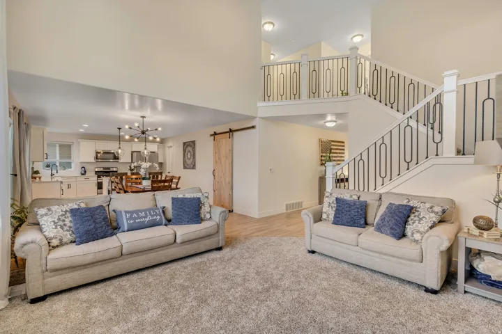Living room with a barn door, hanging lights, a high ceiling, and light colored carpet