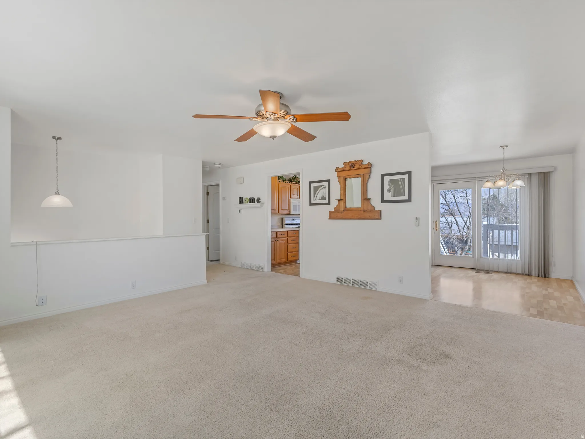 Unfurnished living room featuring light colored carpet, a ceiling fan, and a chandelier