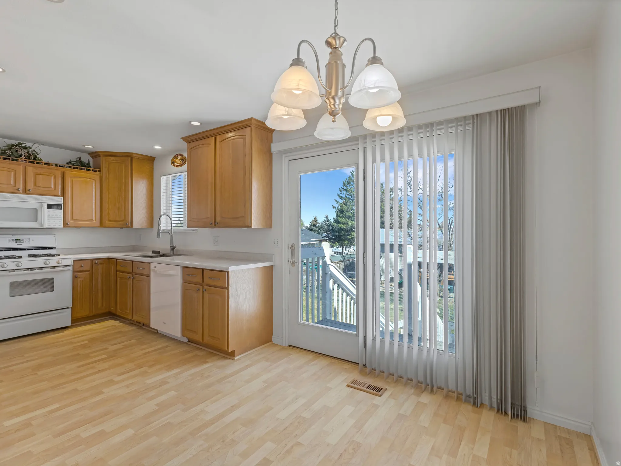 Kitchen with white appliances, a chandelier, light countertops, light wood-style floors, and wood finish cabinets