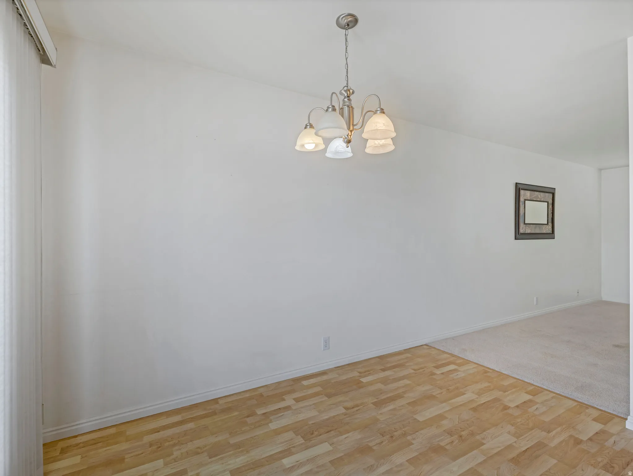 Unfurnished room featuring light wood-type flooring, suspended lighting, and light colored carpet