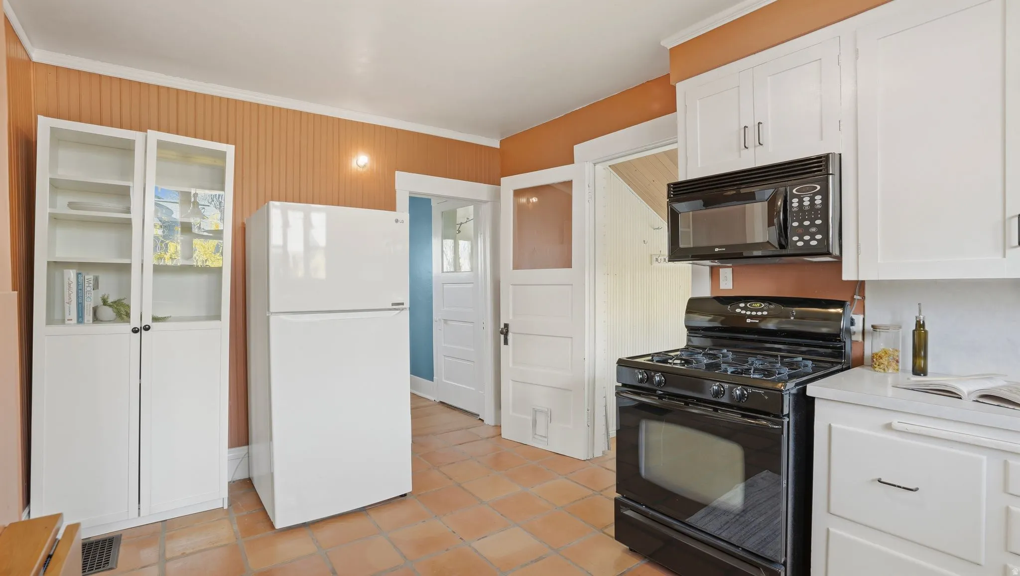 Kitchen with black appliances, white cabinetry, light countertops, crown molding, and light tile patterned flooring