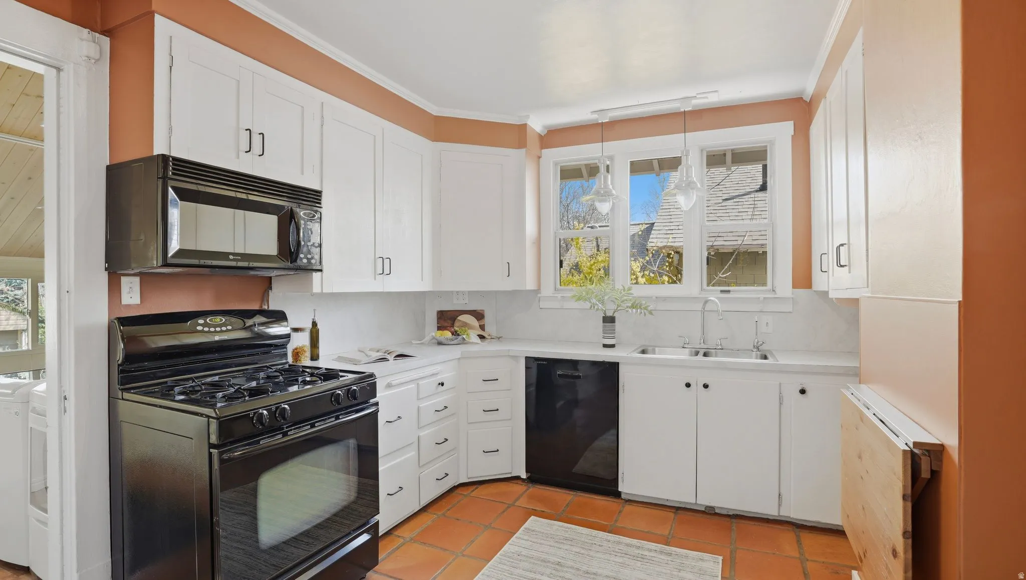Kitchen with black appliances, white cabinetry, light countertops, hanging light fixtures, and ornamental molding