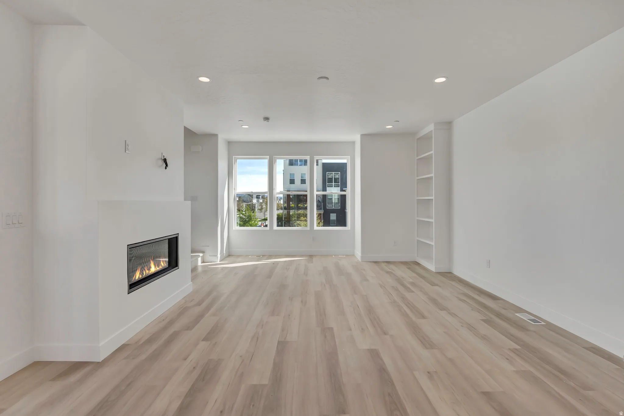 Unfurnished living room featuring light wood-style floors, a glass covered fireplace, and recessed lighting