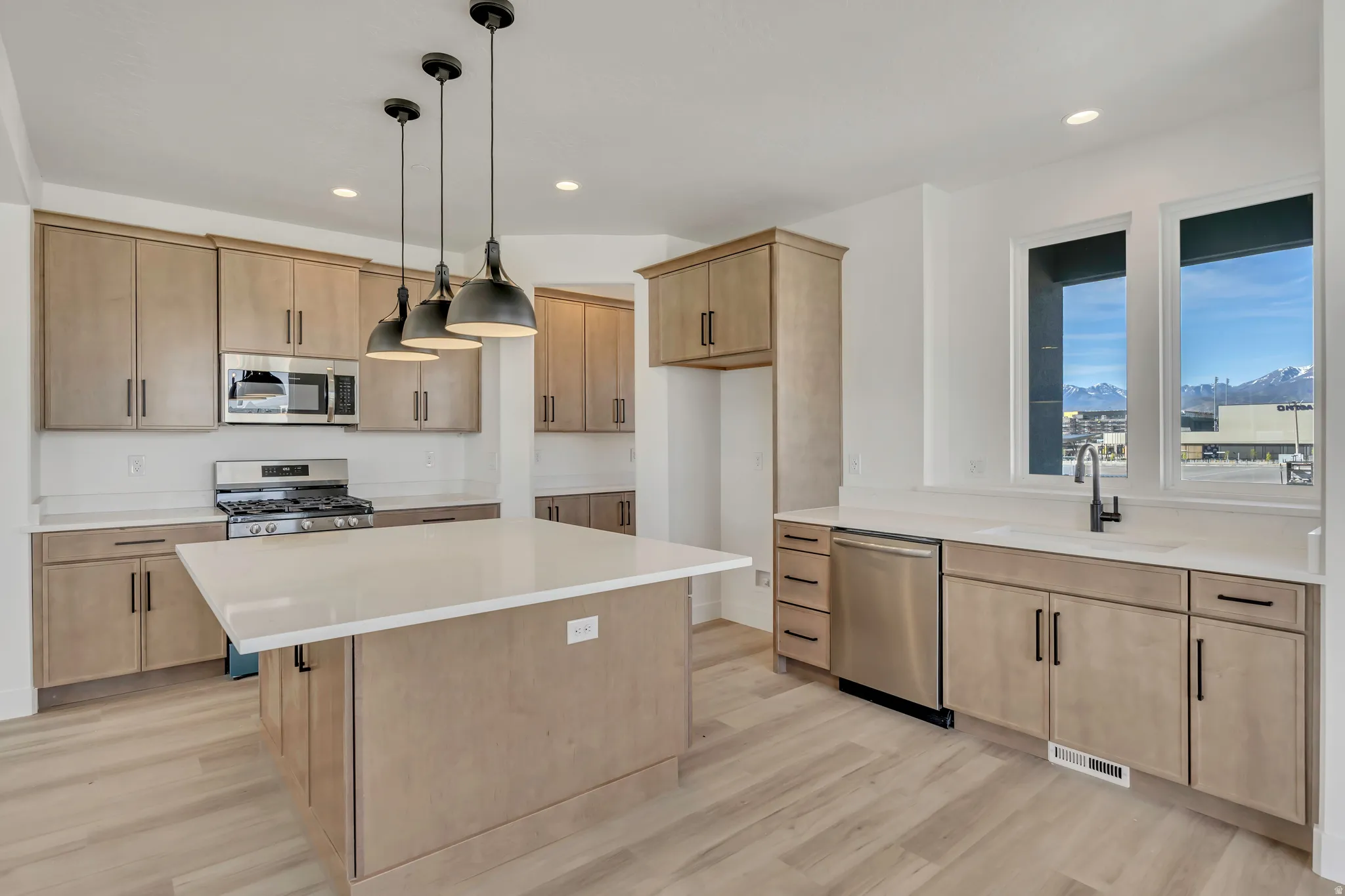 Kitchen featuring light wood finish cabinets, a kitchen island, stainless steel appliances, and light wood finished floors
