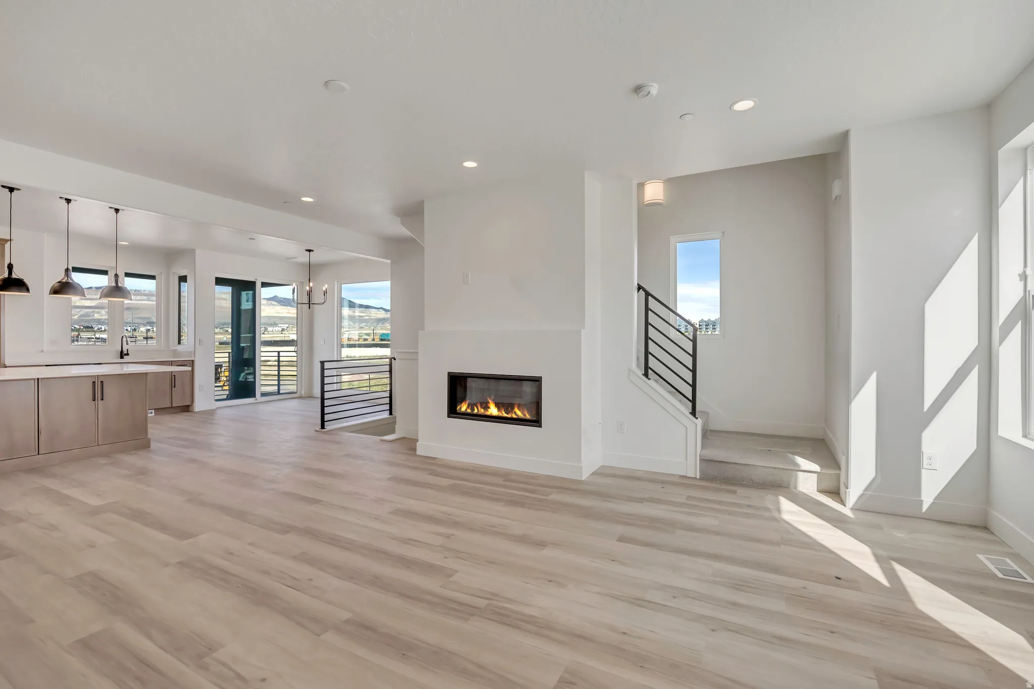 Unfurnished living room featuring a glass covered fireplace, light wood-style flooring, and hanging lights