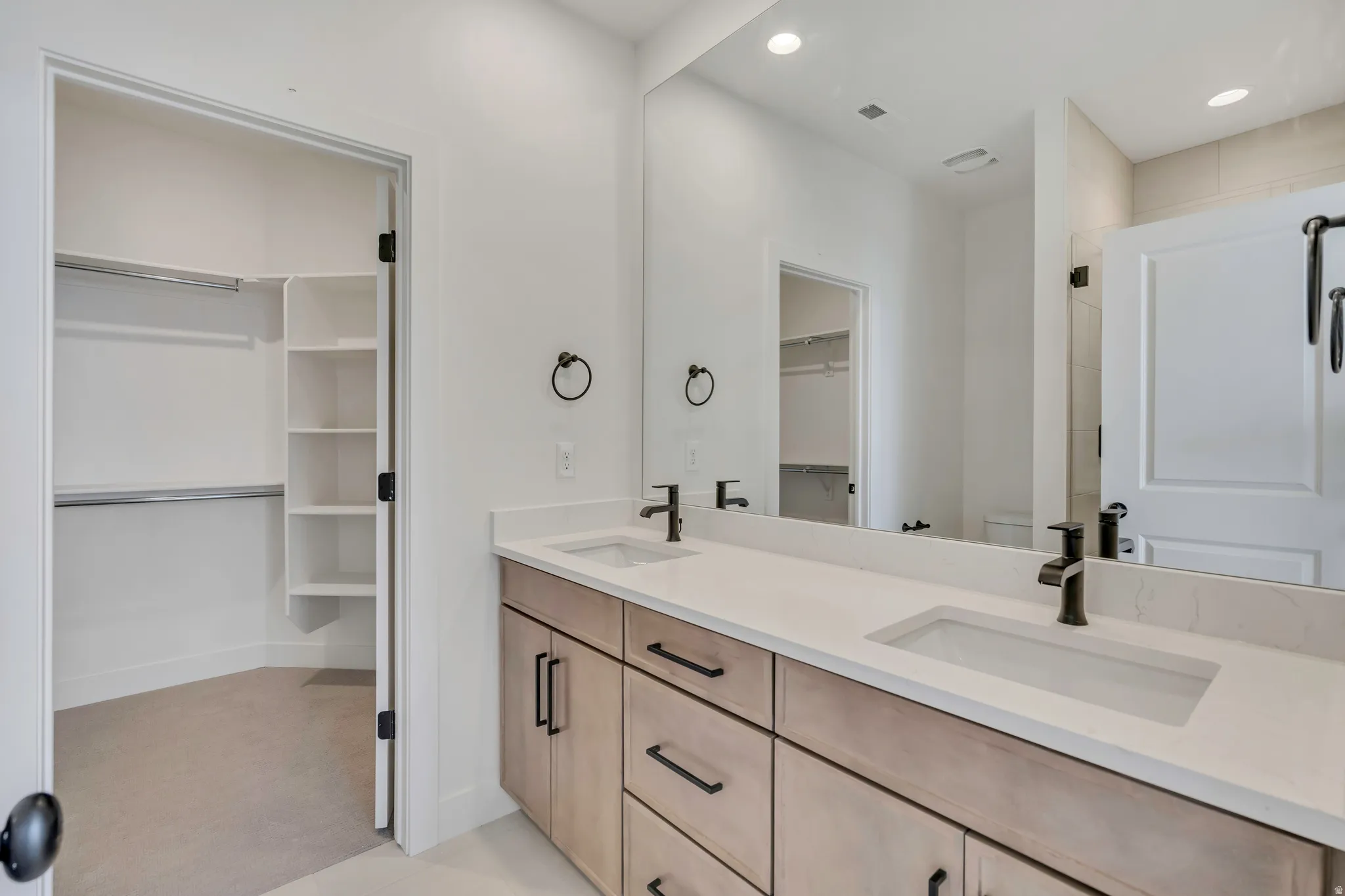 Bathroom featuring a walk in closet, double vanity, recessed lighting, and a shower