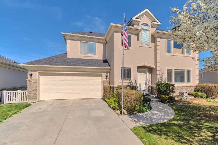 View of front of house featuring stone siding, driveway, a front yard, an attached garage, and stucco siding