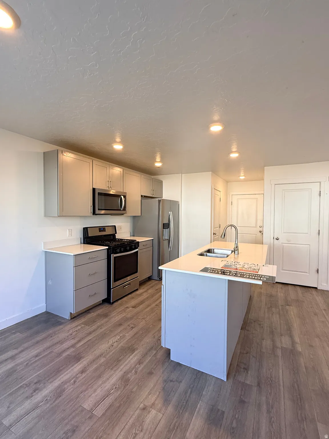 Kitchen featuring gray cabinetry, stainless steel appliances, a center island with sink, dark wood-type flooring, and recessed lighting