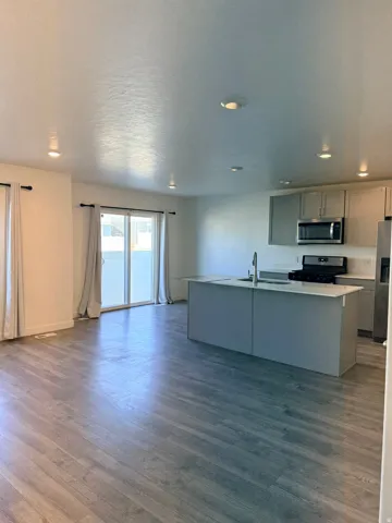 Kitchen with gray cabinets, light countertops, stainless steel appliances, a kitchen island with sink, and dark wood-style flooring
