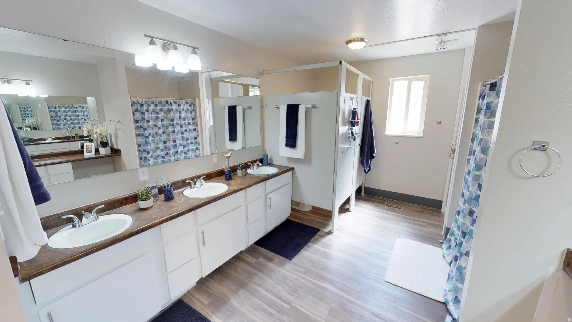 Full bathroom featuring double vanity, light wood-type flooring, and a shower with curtain