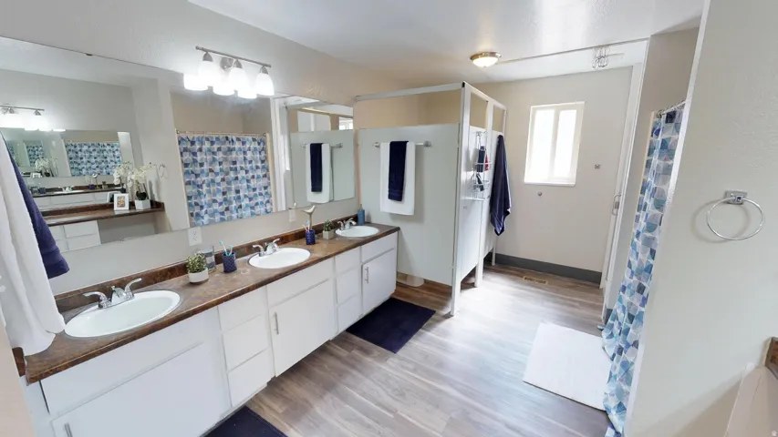 Full bathroom featuring double vanity, light wood-type flooring, and a shower with curtain