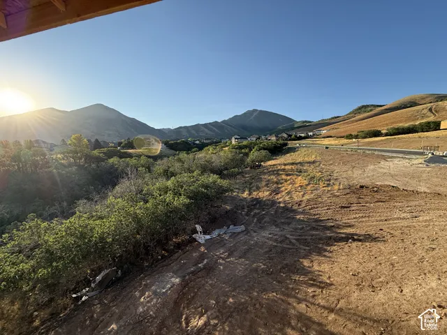 Expansive lot featuring a cleared building site, existing paved road access, and distant mountain scenery