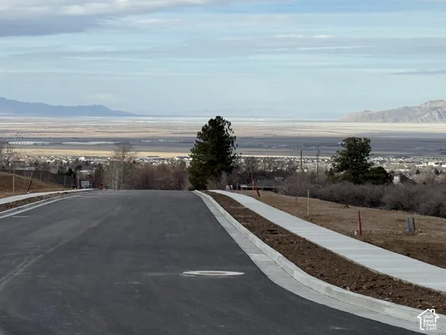 View of asphalt road featuring sidewalks, a mountain view, and curbs