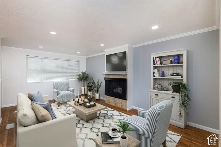 Recessed lighting, wood-finish flooring, corner fireplace with stone surround and mantel, built-in shelving, and crown molding