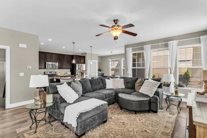 Open concept living space with wood-finish flooring, a ceiling fan with integrated lighting, and multiple windows