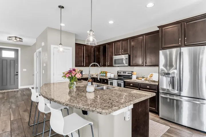 Kitchen featuring dark wood-finish cabinetry, stainless steel appliances, granite countertops, and a central island with a sink and pendant lighting