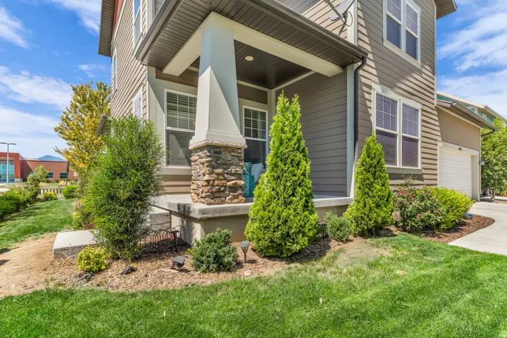 Covered porch with stone-clad column, horizontal siding, attached garage, and manicured landscaping
