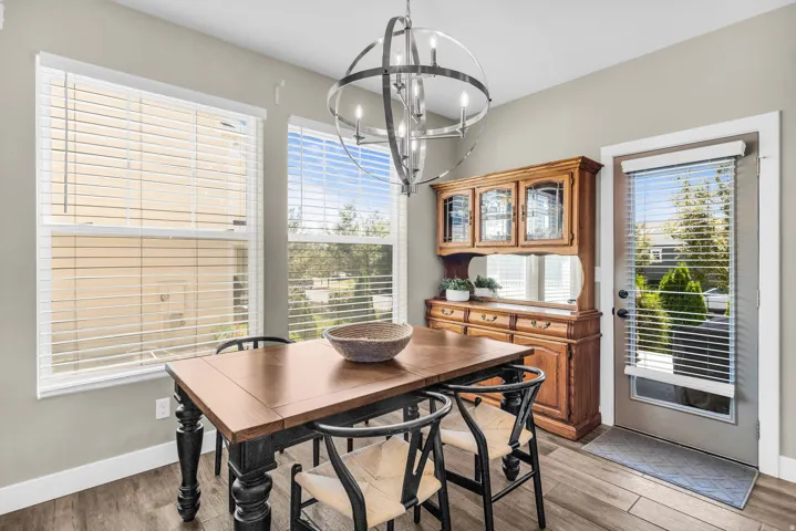 Dining area featuring wood-finish flooring, two large windows with blinds, a glass-paneled exterior door with blinds, and a metal orb chandelier