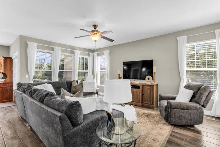 Wood-finish flooring, multiple windows with blinds, ceiling fan, and light neutral wall colors