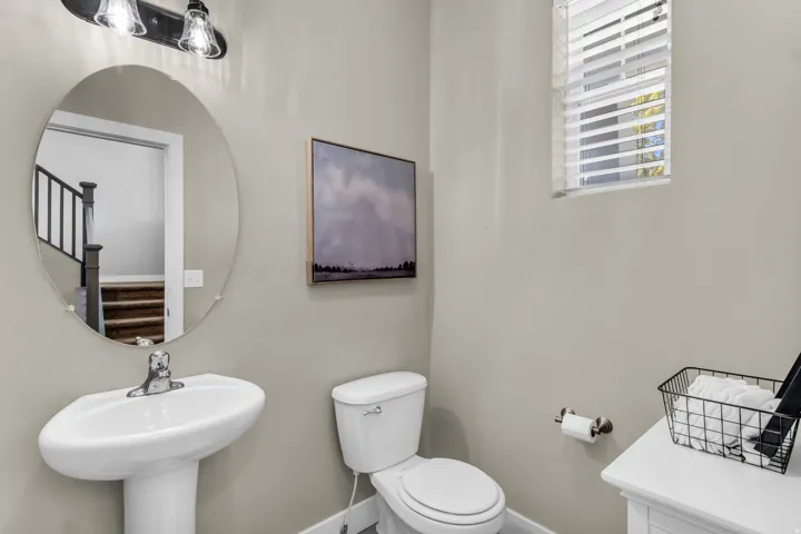 Pedestal sink with chrome faucet, oval wall-mounted mirror, and wall-mounted vanity lighting