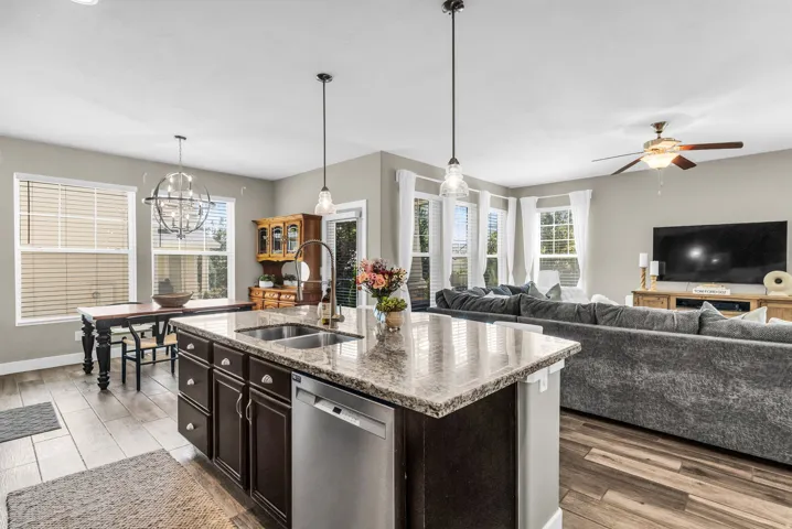Open-concept layout with wood-finish flooring, a kitchen island featuring a dual-basin sink, and recessed lighting