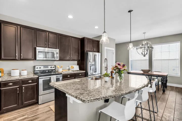 Kitchen featuring dark wood-finish cabinetry, stainless steel appliances, a multi-level island with a sink, and wood-finish flooring