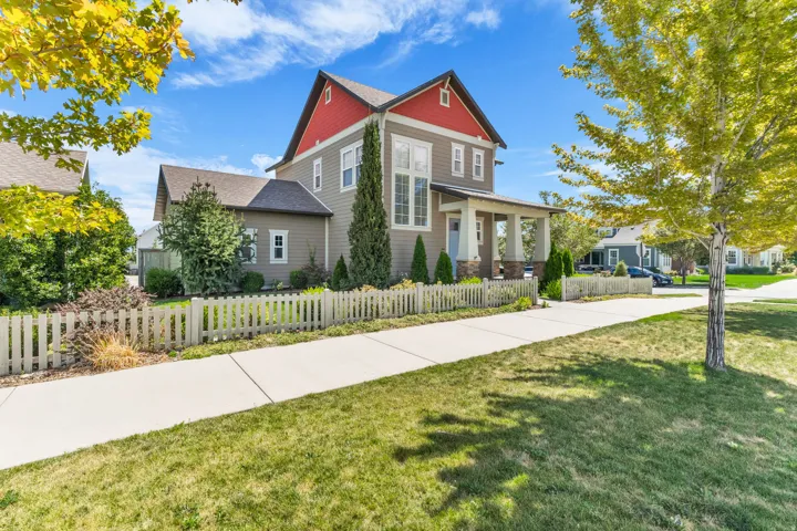 Two-story residence featuring a covered front porch, a white picket fence, and mature landscaping