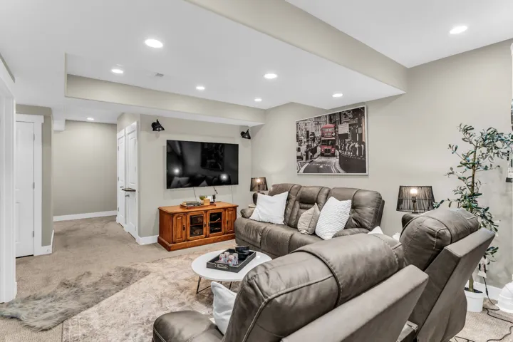 Recessed ceiling lighting, wall-mounted television, wood-finish media console, and built-in closet storage