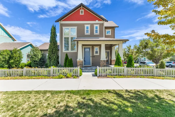 Multi-story residence featuring a covered front porch with stone accents, a prominent gable with red siding, and white picket fencing