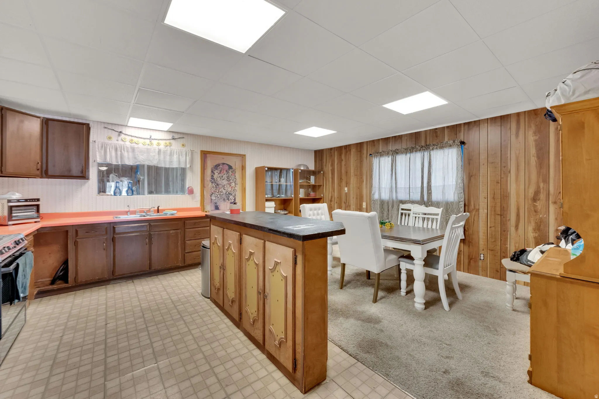 Kitchen with plenty of natural light, light floors, a drop ceiling, a center island, and wood walls