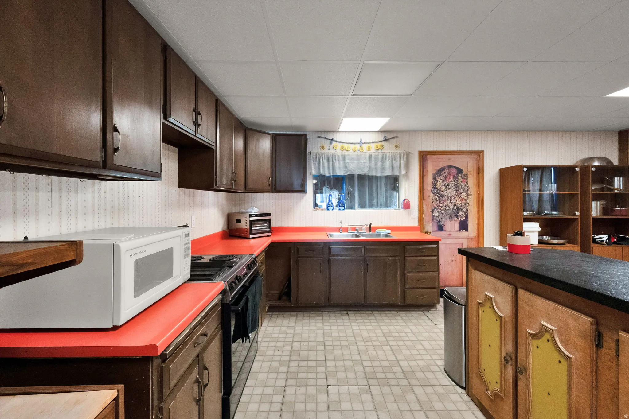 Kitchen with dark wood finish cabinetry, white microwave, light floors, wallpapered walls, and black electric range oven