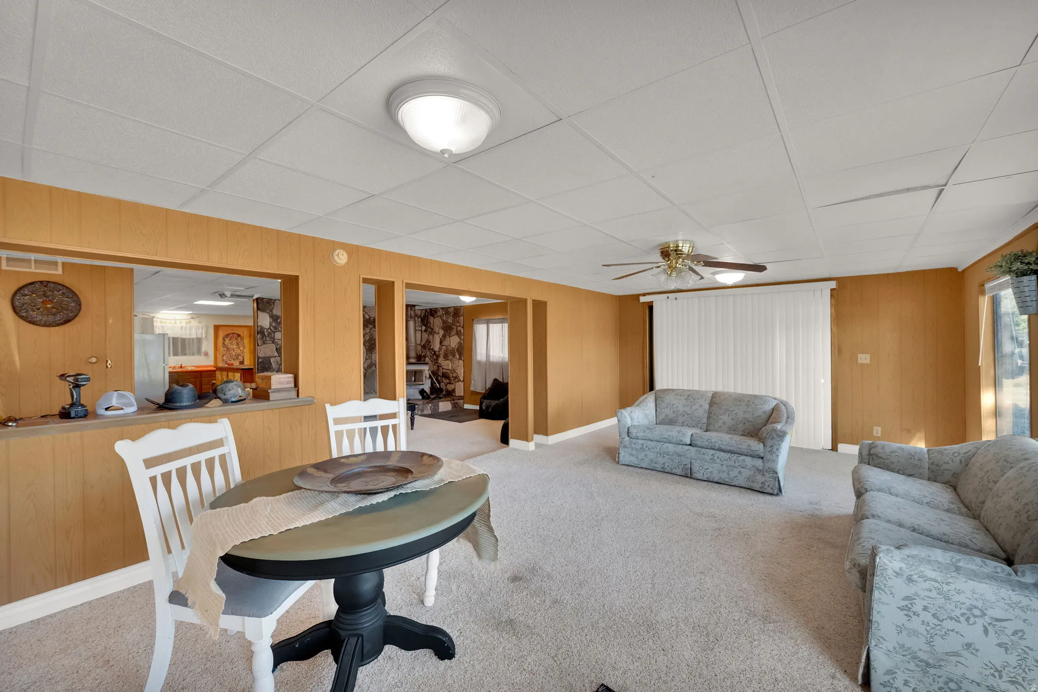 Living room featuring carpet flooring, wooden walls, ceiling fan, and a drop ceiling