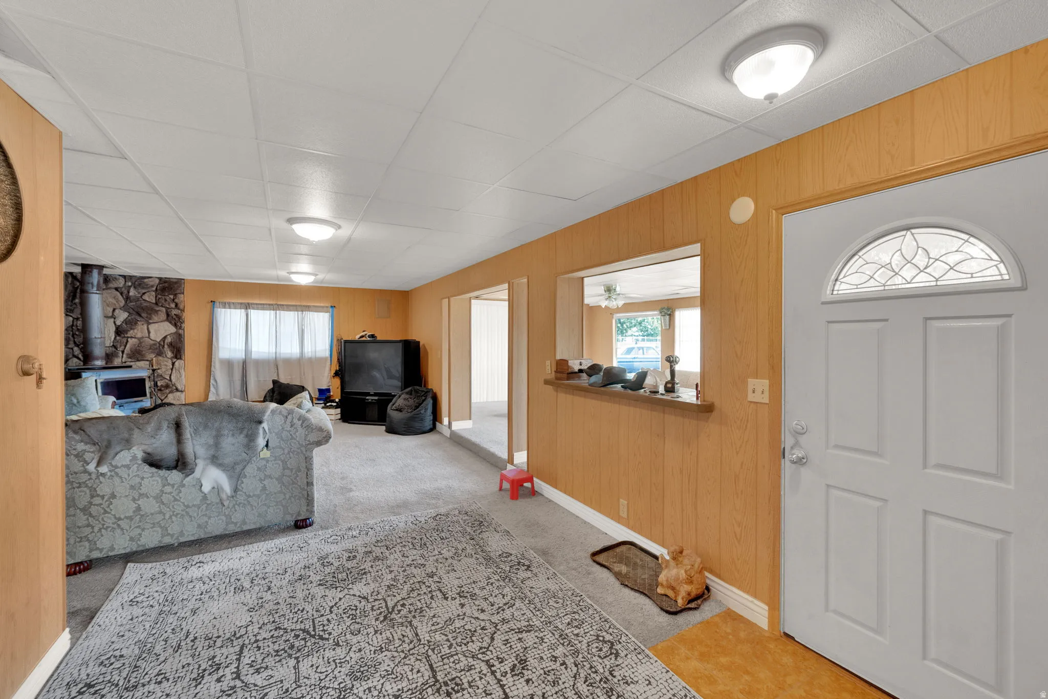 Entrance foyer featuring a wood stove, wood walls, light colored carpet, and a paneled ceiling