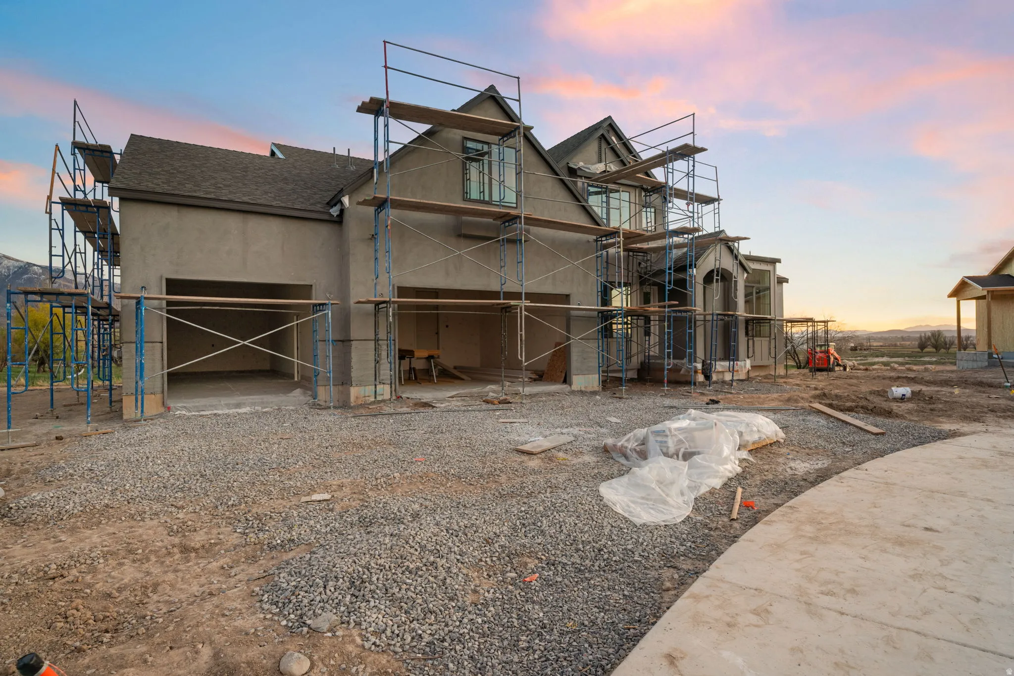 Back of house at dusk featuring a shingled roof, driveway, and stucco siding