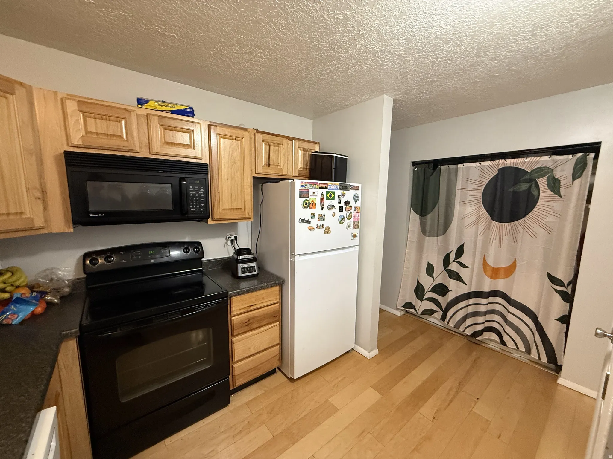 Kitchen featuring black appliances, dark countertops, light wood-style flooring, and light wood finish cabinets