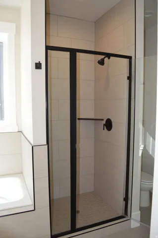 Shower with clear glass enclosure and matte black frame, tile shower surround, and a built-in shower shelf