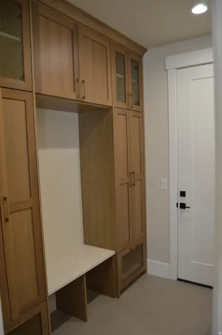 Built-in wood-finish cabinetry featuring glass-front doors, integrated bench with a light-toned solid surface top, and recessed ceiling lighting