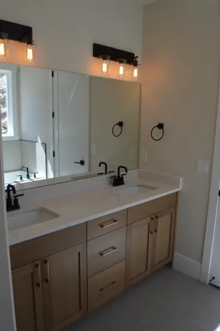 Dual vanity with light wood-finish cabinetry, gold-tone hardware, and white countertops