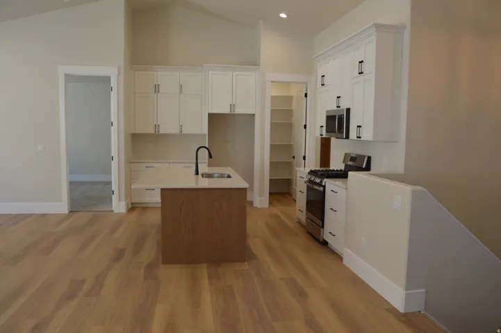 Kitchen featuring a center island, wood-finish flooring, white cabinetry with dark hardware, stainless steel appliances, and a dedicated pantry