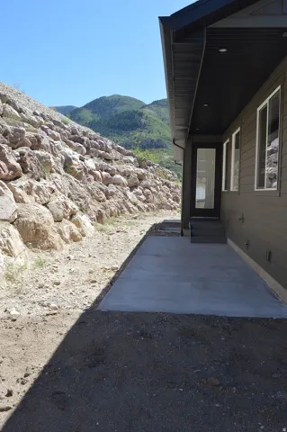 Exterior featuring dark siding, multiple windows, a concrete patio, and a mountain backdrop