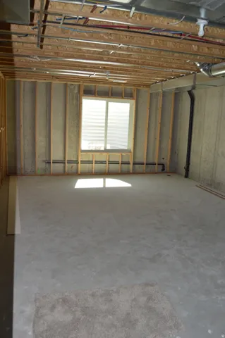 Unfinished basement featuring exposed wood ceiling joists, concrete walls, a large window, and a concrete floor