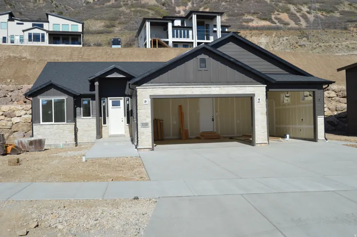 View of front facade featuring stone siding, board and batten siding, a garage, and driveway