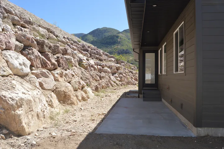 Exterior wall cladding, multiple windows, a glass-paneled door, and a concrete patio