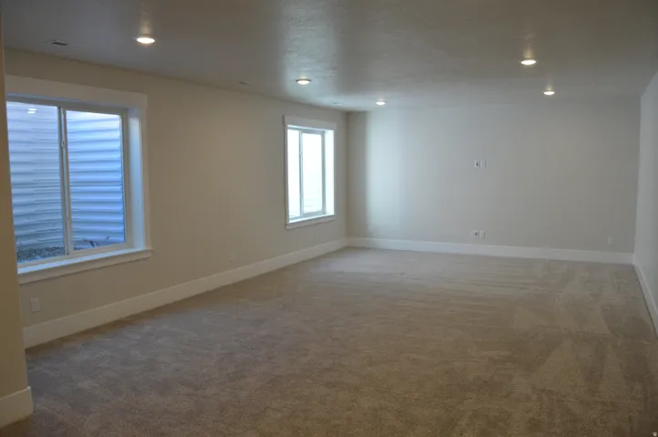 Spacious room featuring neutral carpeting, recessed lighting, and two windows with white trim