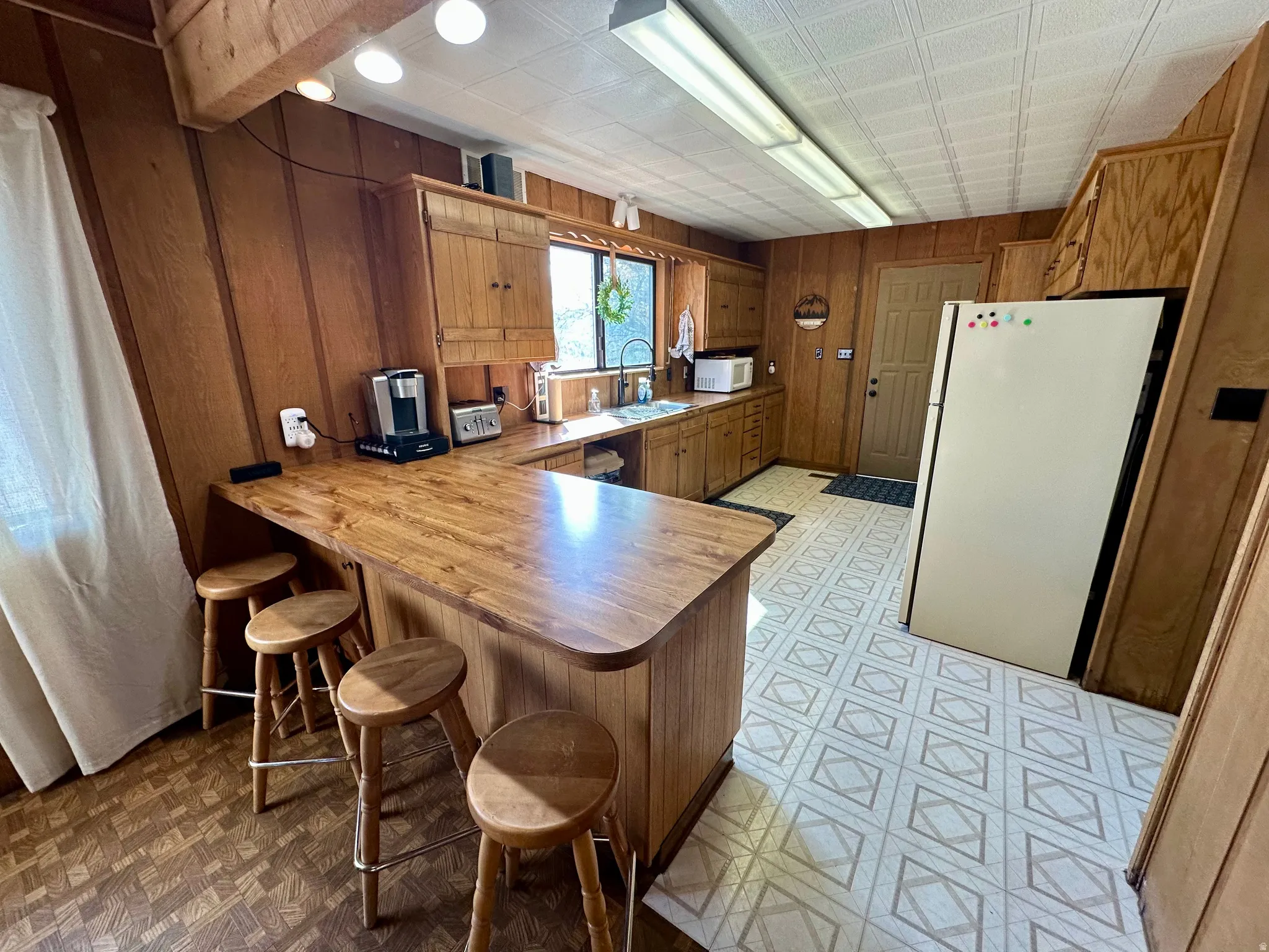 Kitchen featuring wood finish cabinetry, a peninsula, white appliances, a kitchen breakfast bar, and wooden walls